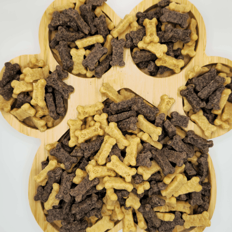 Artful display of Gentle Berry Bites by Glamorous Pups on a wooden paw print-shaped serving board. This arrangement features nutritious dog treats in bone shapes, presented in contrasting colors of light beige and dark brown. The unique and appealing presentation underscores Glamorous Pups’ commitment to high-quality, natural ingredient dog treats, ideal for rewarding and training.