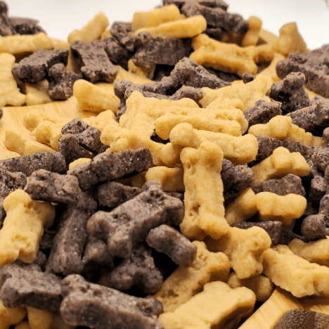 Close-up of Gentle Berry Bites by Glamorous Pups displayed on a wooden paw print-shaped serving board. The dog treats, shaped like bones, come in contrasting colors of light beige and dark brown, highlighting their all-natural ingredients and appeal. This presentation emphasizes the brand's commitment to providing high-quality, nutritious treats for dog training and healthy snacking.