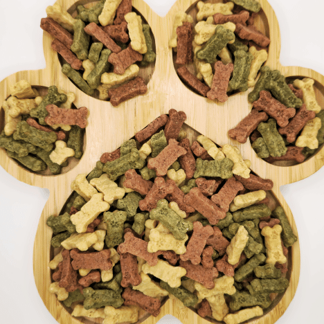 Image showcasing an assortment of Frostbite Fruity Snacks Dog Treats by Glamorous Pups, displayed on a paw-shaped wooden platter. These treats come in various colors and shapes, appealing to pet owners looking for visually engaging and nutritious snacks for their dogs.