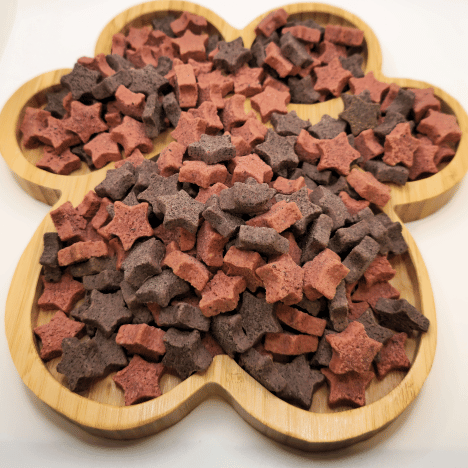 Galactic Berry Gems Dog Treats by Glamorous Pups artfully displayed on a wooden paw-shaped platter. These treats are shaped as stars and bones, crafted from high-quality ingredients like blueberries and cranberries, perfectly designed to provide both nutrition and taste for your pet.