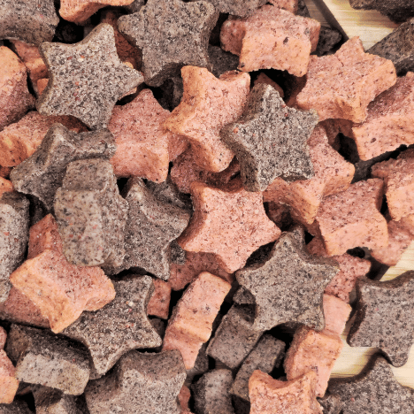 Close-up view of Galactic Berry Gems Dog Treats by Glamorous Pups, featuring an array of star and bone-shaped treats in shades of pink and gray. These premium dog treats are made from natural ingredients including blueberries and cranberries, perfect for pet owners seeking healthy, flavorful options for their dogs.