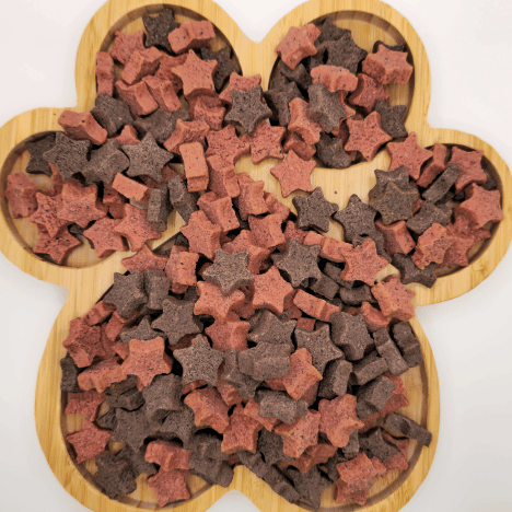 Close-up display of Galactic Berry Gems Dog Treats by Glamorous Pups, artistically arranged on a wooden paw-shaped board. These star and bone-shaped treats are crafted with a blend of nutrient-rich ingredients, offering a delicious and healthy choice for your furry friends.