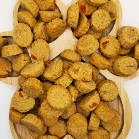 Close-up view of Tropical Pupaya Paradise Dog Treats by Glamorous Pups, artfully displayed on a paw-shaped wooden board. Each treat, crafted with flavors of pineapple and papaya, showcases a unique, appetizing texture, perfect for dog owners seeking nutritious and exotic snack options for their pets.