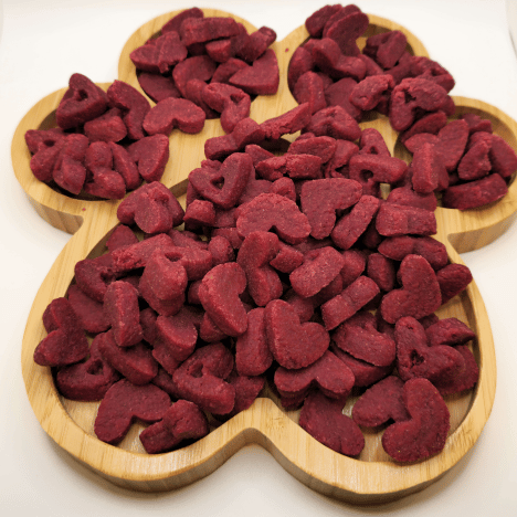 Display of heart-shaped Velvet Love Whispers Dog Dog Treats by Glamorous Pups on a wooden paw-shaped board, highlighting the vibrant red velvet color. These gourmet dog treats are ideal for showing love to your pet, crafted with high-quality ingredients to ensure delicious and nutritious snacks.