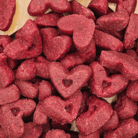 Close-up view of Velvet Love Whispers Dog by Glamorous Pups, showcasing the rich red velvet color in heart shapes, perfect for treating your cherished canine. These premium dog snacks, featured on a wooden background, are made with natural ingredients to promote pet health and happiness.