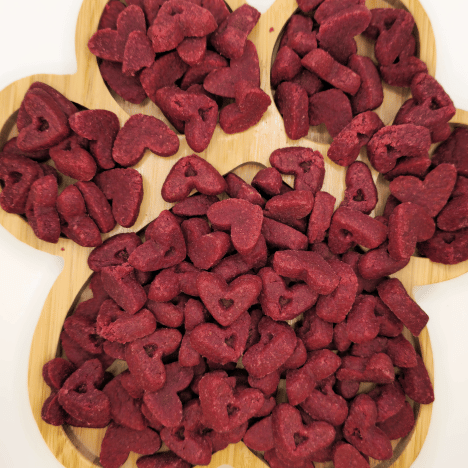 Top view of Pup's Love Kisses Dog Treats by Glamorous Pups, artfully arranged on a wooden board shaped like a flower. These heart-shaped, red velvet flavored treats are ideal for rewarding your furry friend, crafted with wholesome ingredients for your dog's delight.