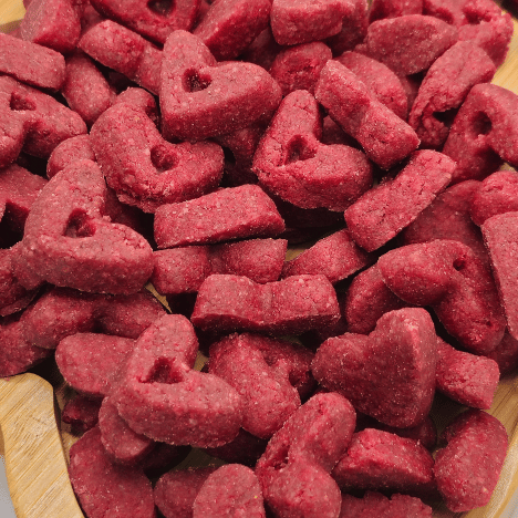 Delicious Velvet Love Whispers Dog Treats by Glamorous Pups displayed on a wooden board, featuring vibrant red, heart-shaped pieces perfect for rewarding and treating dogs with a taste of luxury.