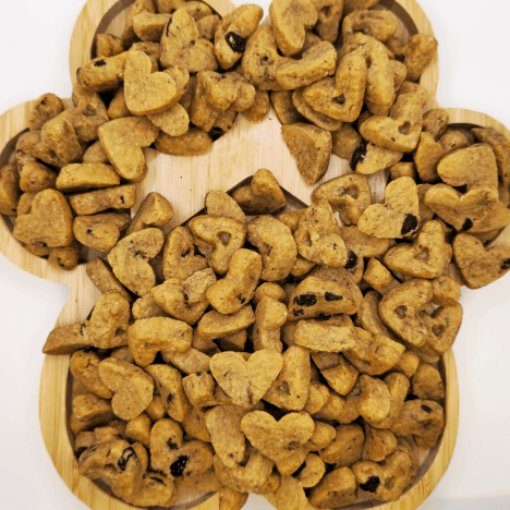 Artful arrangement of Peanut Butter Pup Dog Treats by Glamorous Pups on a wooden board shaped like a dog's paw, showcasing the delightful heart and bone shapes of these nutritious snacks, perfect for dog owners seeking healthy, made-in-the-USA treats with real peanut butter flavor.