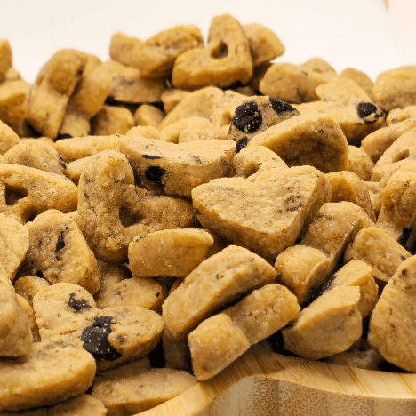 Close-up view of Peanut Butter Pup Dog Treats by Glamorous Pups, featuring a mix of heart-shaped and bone-shaped biscuits with visible chunks of peanut, arranged on a paw-print shaped wooden board, perfect for pet owners looking for tasty, all-natural treats made in the USA.