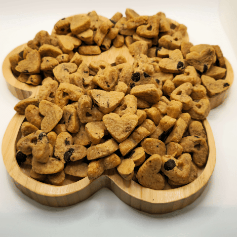 Display of Peanut Butter Pup Dog Treats by Glamorous Pups arranged on a paw print-shaped wooden serving board, showcasing their unique shapes and rich textures. This premium pet snack emphasizes its peanut butter flavor, highlighted with visible chunks of ingredients, ideal for pet owners seeking healthy and delicious treats for their dogs.