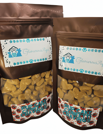 Two resealable bags of Pup Cake Confetti Cravings Dog Treats by Glamorous Pups, presented in glossy brown packages with transparent windows showcasing the heart-shaped, confetti-like treats inside. Each bag features the Glamorous Pups logo surrounded by blue paw prints, and the product name 'Pup Cake Confetti Cravings' prominently displayed, emphasizing the treats' fun and festive appeal. These gourmet dog treats are perfect for owners seeking nutritious, made-in-the-USA snacks for their pets.