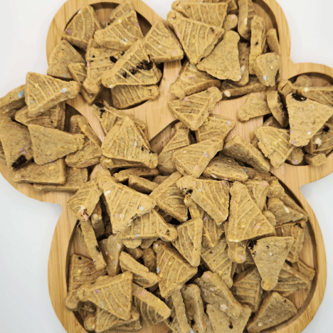 Delicious Banana Bash Caps Dog Treats displayed on a bamboo paw-shaped serving board by Glamorous Pups. These premium dog treats, shaped like triangular caps, offer a healthy, tasty snack option for dogs, made with natural banana ingredients, enhancing appeal for pet owners seeking gourmet treat options for their pets.