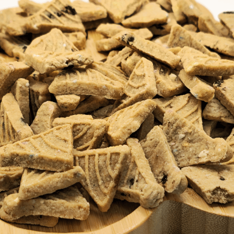 Close-up of Banana Bash Caps Dog Treats by Glamorous Pups, showcasing the unique triangular shape and delicious texture. Made with natural banana flavor, these artisan treats are laid out on a bamboo paw-shaped board, highlighting the quality and appeal of these healthy dog snacks.