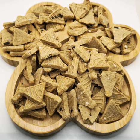 Scrumptious Banana Bash Caps Dog Treats arranged on a bamboo paw print-shaped serving board by Glamorous Pups. These artisanal dog treats, crafted in triangular shapes, are perfect for pets and designed with natural banana flavors to satisfy a dog’s taste buds while providing a fun, gourmet snacking experience for furry friends.