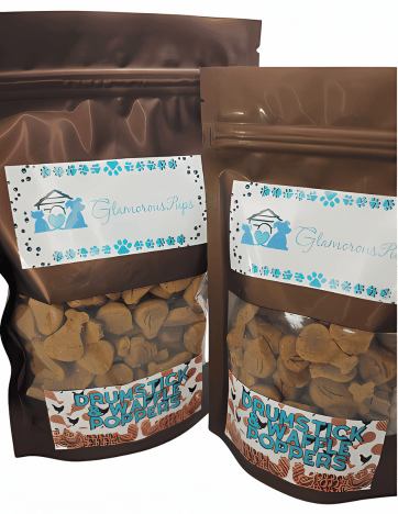 Two resealable bags of Drumstick & Waffle Poppers Dog Treats by Glamorous Pups, each featuring glossy brown packaging with a clear viewing window that showcases the uniquely shaped treats resembling drumsticks and waffles. The bags are labeled with the Glamorous Pups logo and decorative blue paw prints, emphasizing the treats' gourmet, all-natural ingredients. This product is ideal for pet owners looking to indulge their dogs with fun, tasty, and nutritious snacks made in the USA.