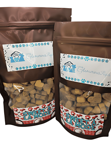 Two bags of Sweet À La Mode Dog Treats by Glamorous Pups, each in a glossy brown resealable package with a clear window displaying uniquely shaped treats inside. The labels, adorned with the Glamorous Pups logo and blue paw prints, feature the product name 'Sweet À La Mode' in attractive, festive typography. These gourmet dog treats are crafted to appeal to pet owners seeking high-quality, delicious snacks for their pets, made with all-natural ingredients in the USA.