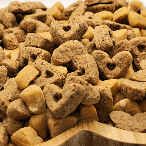 Close-up of Sweet À La Mode Dog Treats by Glamorous Pups, displayed on a wooden paw print-shaped serving board. The treats are in heart and bone shapes, featuring a rich, textured surface in shades of golden brown, emphasizing their natural and wholesome ingredients. Perfect for dog owners seeking gourmet, nutritious snacks for their pets, these treats are crafted with high-quality, all-natural ingredients and are proudly made in the USA.