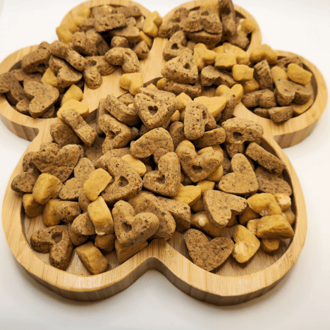 Sweet À La Mode Dog Treats by Glamorous Pups, artistically displayed on a wooden paw print-shaped board. The assortment includes treats shaped like hearts and bones in varying shades of golden brown, showcasing their wholesome and natural composition. These gourmet treats cater to pet owners seeking creative, high-quality, nutritious snacks for their dogs, highlighting Glamorous Pups' commitment to all-natural ingredients and made-in-the-USA quality.