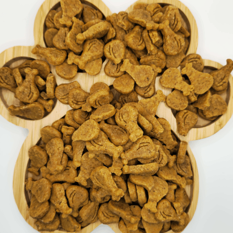 Drumstick & Waffle Poppers Dog Treats by Glamorous Pups, displayed on a wooden paw print-shaped serving board. The treats, shaped like mini drumsticks and waffles, are densely piled to showcase their unique forms and appealing texture. Made with all-natural ingredients, these treats are designed for pet owners looking for fun, nutritious, and high-quality snacks for their dogs, crafted with care in the USA.