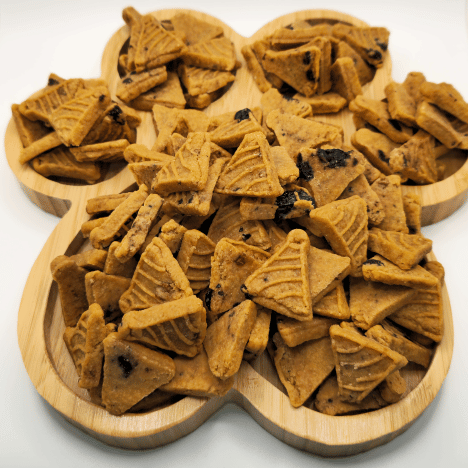 Assorted Blueberry Pupcake Party treats by Glamorous Pups, displayed on a wooden paw print-shaped serving board. The treats are crafted into delightful pancake shapes with visible blueberry pieces, emphasizing their all-natural, tasty ingredients. This presentation showcases the unique and healthy snack options available for dogs, ideal for owners looking for nutritious, made-in-the-USA treats.