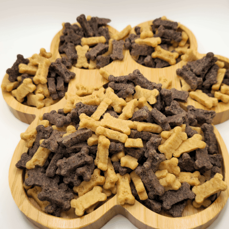 Eye-catching display of Gentle Berry Bites by Glamorous Pups, arranged on a wooden paw print-shaped serving board. The image showcases a variety of bone-shaped dog treats in light beige and dark brown, illustrating the quality and appeal of these nutritious, natural ingredient snacks, designed for pet training and rewarding.