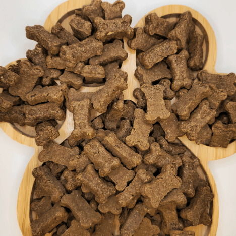 Aromatic Savory Bacon Bliss Dog Treats by Glamorous Pups, artistically arranged on a paw-shaped wooden board, featuring bone and stick shapes, highlighting their gourmet, bacon-infused formula crafted for dog indulgence.