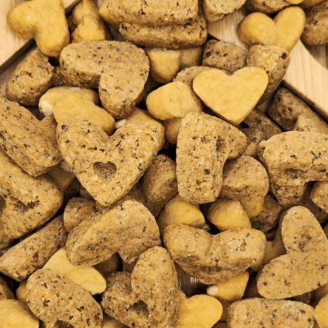 Sweet À La Mode Dog Treats by Glamorous Pups, creatively arranged on a wooden surface. The treats are shaped like hearts and bones, colored in contrasting shades of golden yellow and speckled gray, showcasing their wholesome, natural ingredients. These gourmet treats are perfect for pet owners looking for high-quality, nutritious snacks, made with all-natural ingredients and lovingly crafted in the USA.